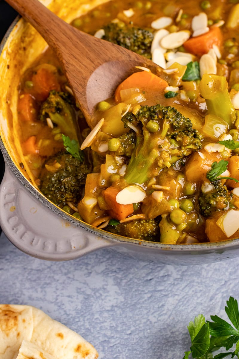 close up wooden spoon scooping out some 30-minute vegetable korma from pot