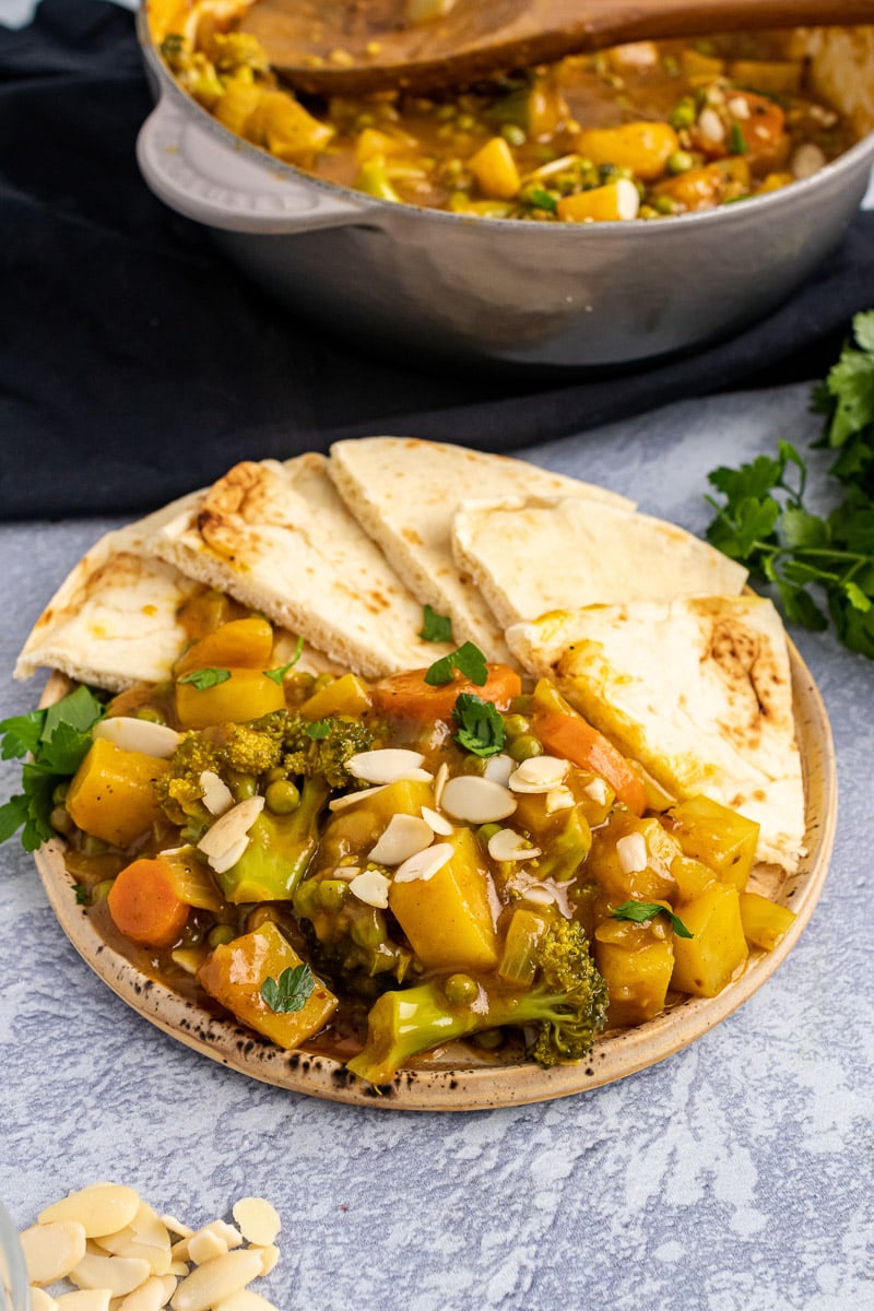 plate of 30-minute vegetable korma on plate with naan bread and pot of korma in background