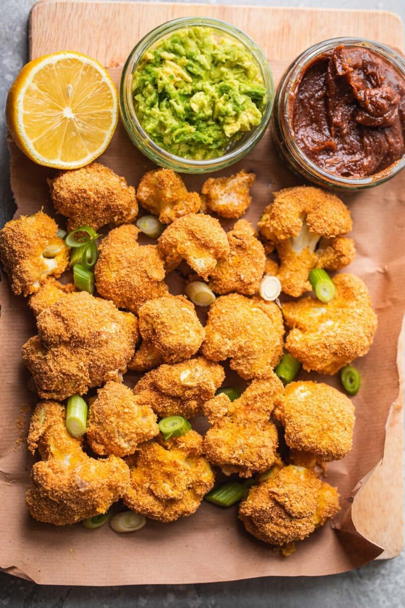 Breaded cauliflower on a wooden board with mashed avocado and almond dip