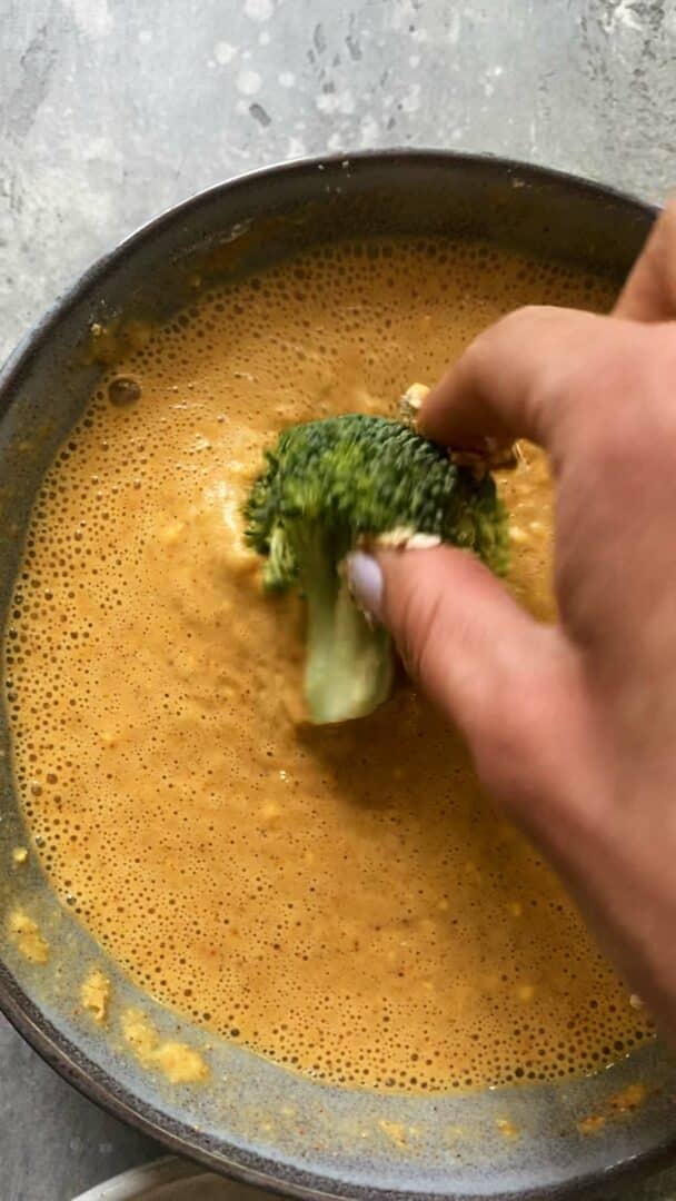 Broccoli being dipped into batter