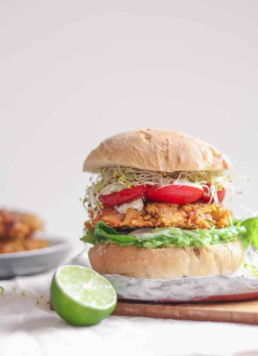 Vegan chickpea fritter sandwich with avocado, mixed greens, tomatoes, soy yoghurt and alfalfa sprouts 