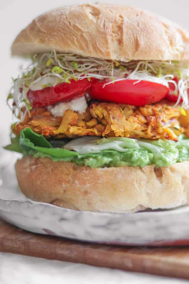 Closeup of Vegan chickpea fritter sandwich with avocado, mixed greens, tomatoes, soy yoghurt and alfalfa sprouts 