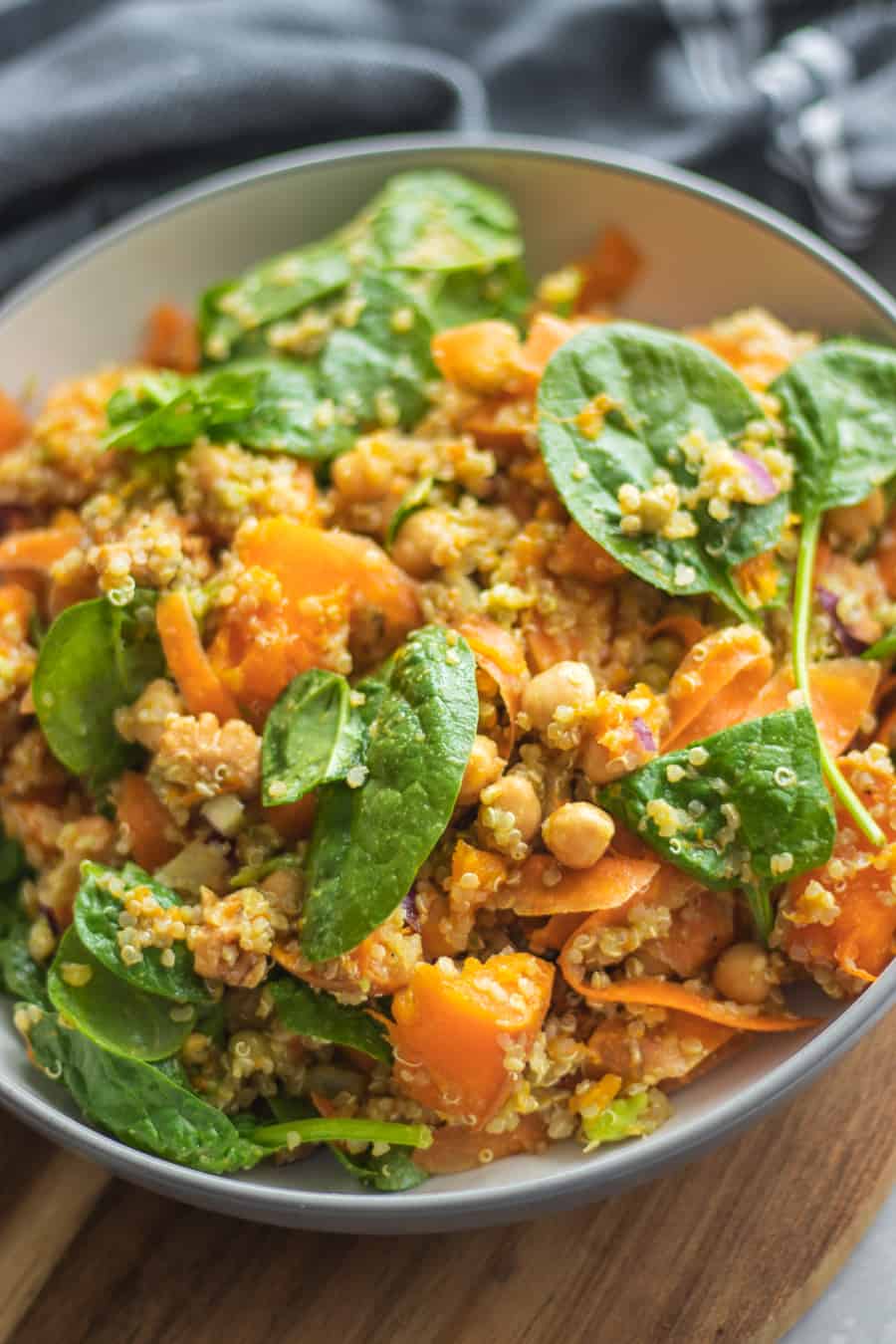 Warm pumpkin quinoa salad with chickpeas, carrot ribbons and baby spinach in a white bowl
