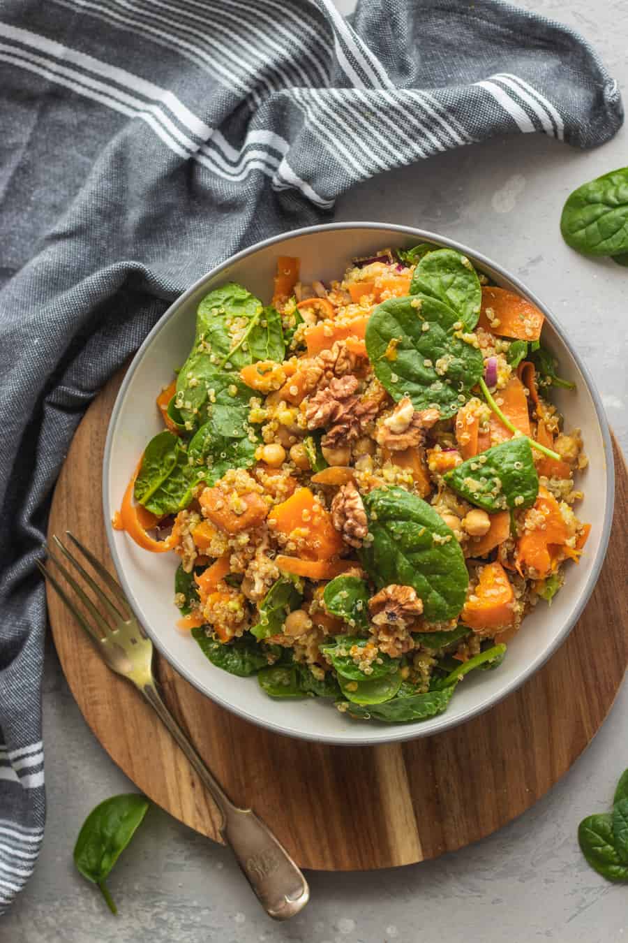 Pumpkin chickpea quinoa bowl on a wooden board with a fork and a striped napkin