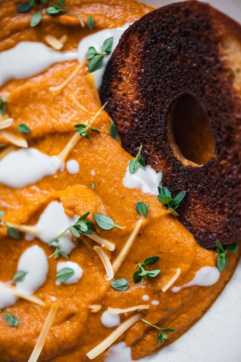 Closeup of a bowl of sweet potato soup with a bagel