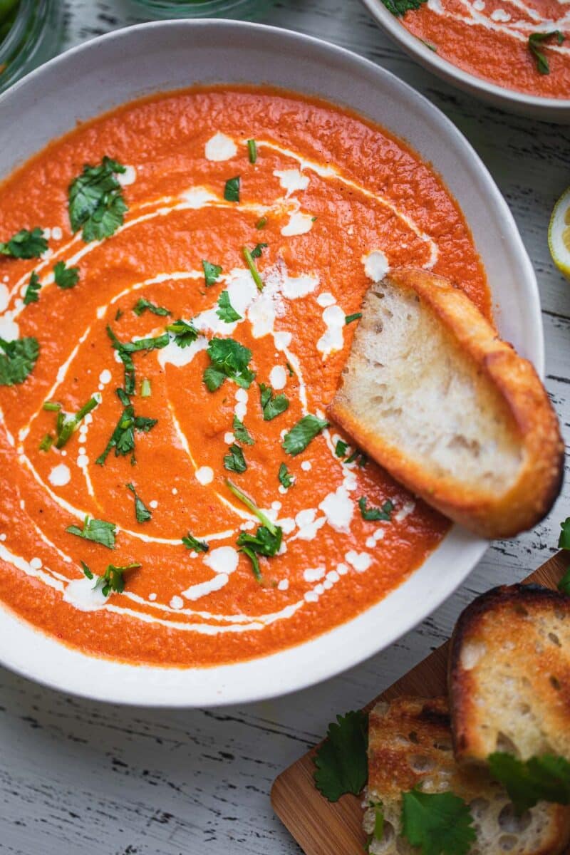 Closeup of a bowl of vegan tomato soup with bread and cilantro