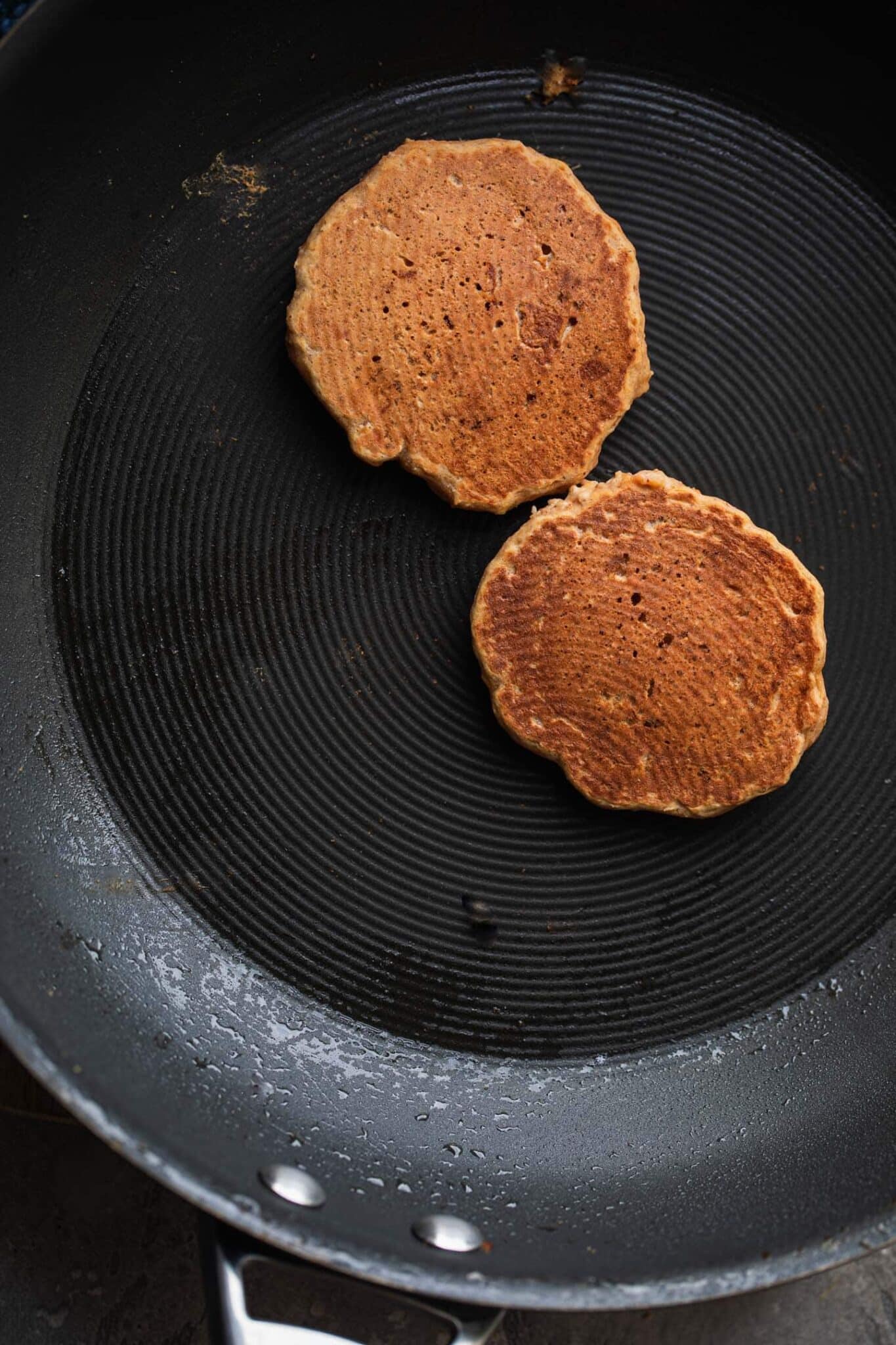 Two golden pumpkin pancakes flipped in a frying pan