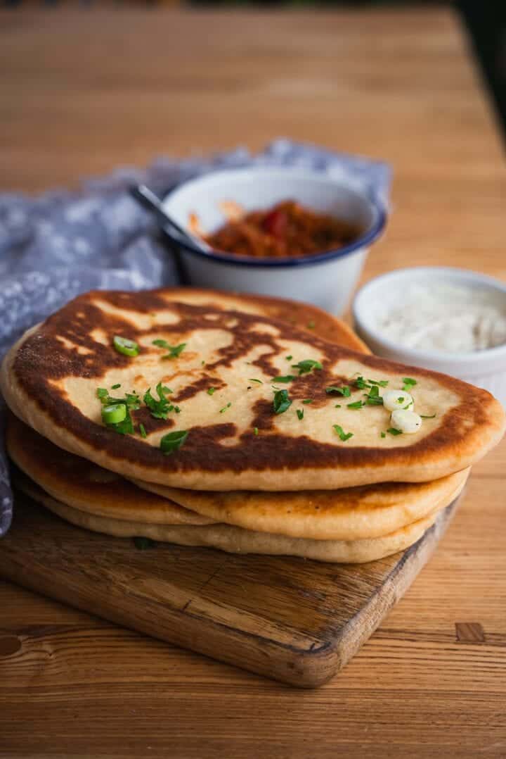 Eggless naan bread resting on a table next to curry and yogurt