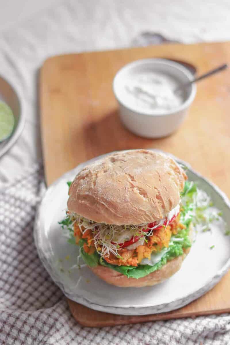 Vegan fritter sandwich with avocado, mixed greens, alfalfa sprouts, panfried tomatoes, soy yoghurt and alfalfa sprouts resting on a table