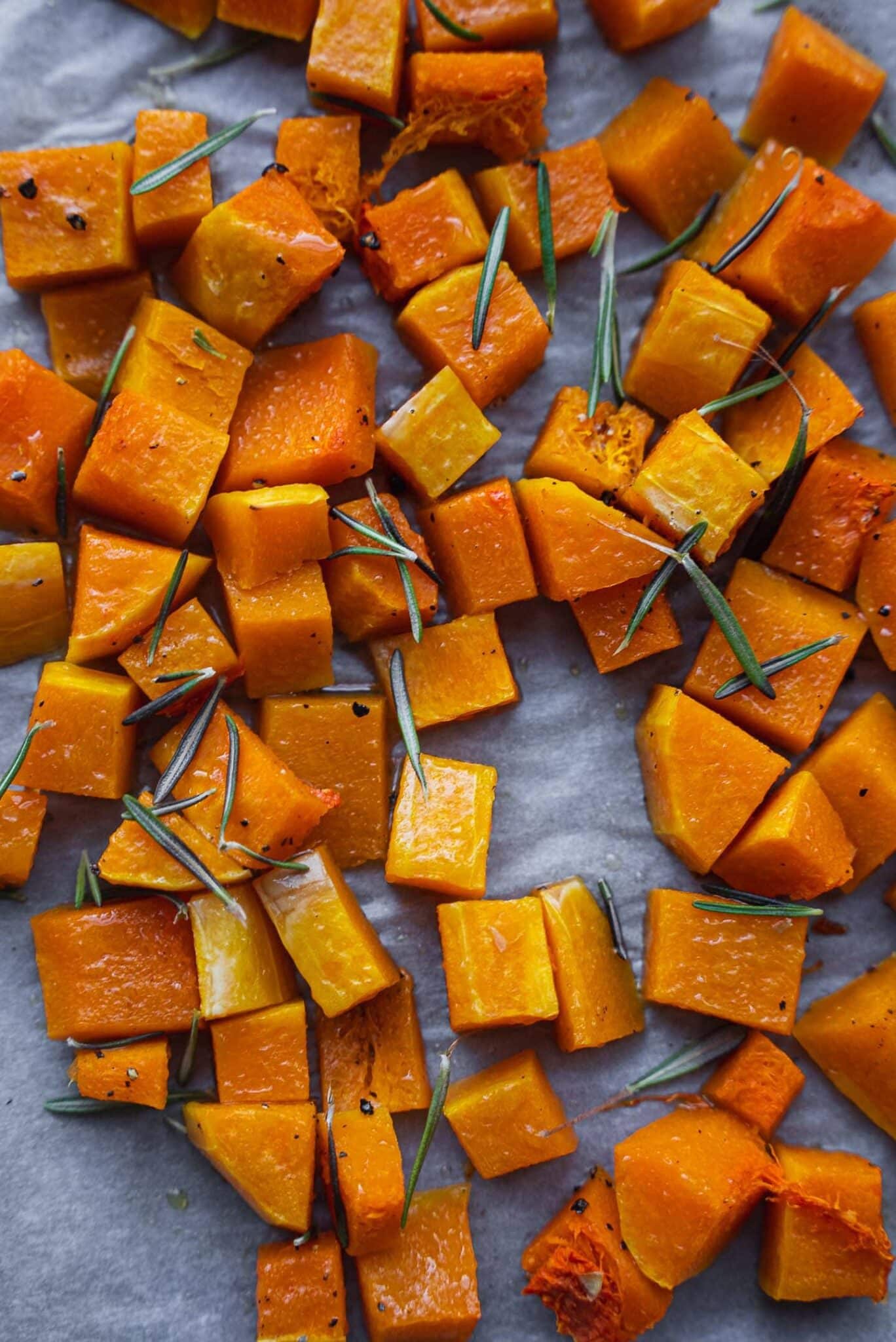 Roasted butternut squash cubes with rosemary on a baking tray
