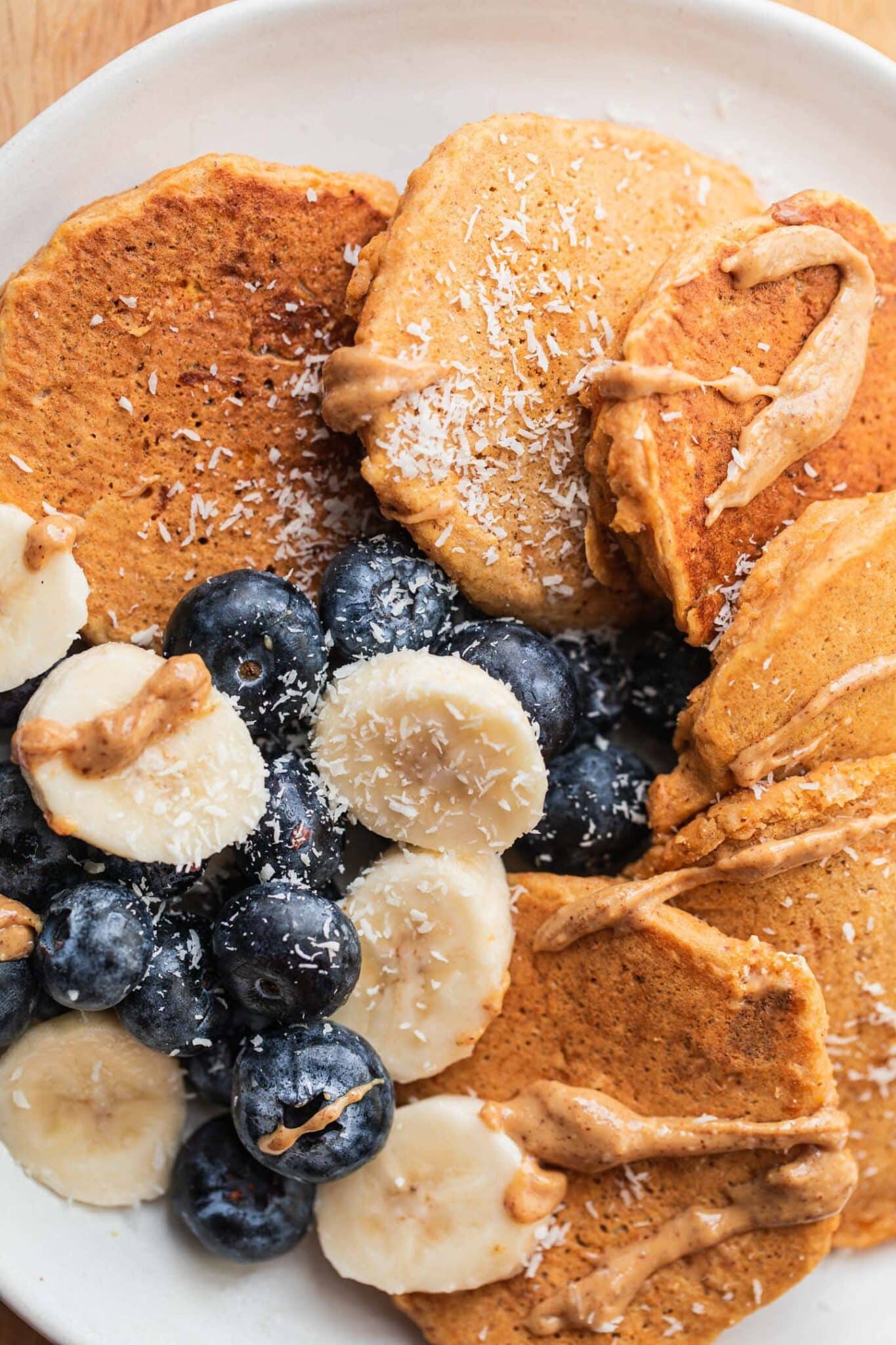 Plate of gluten-free vegan pumpkin pancakes with blueberries and banana on a wooden board