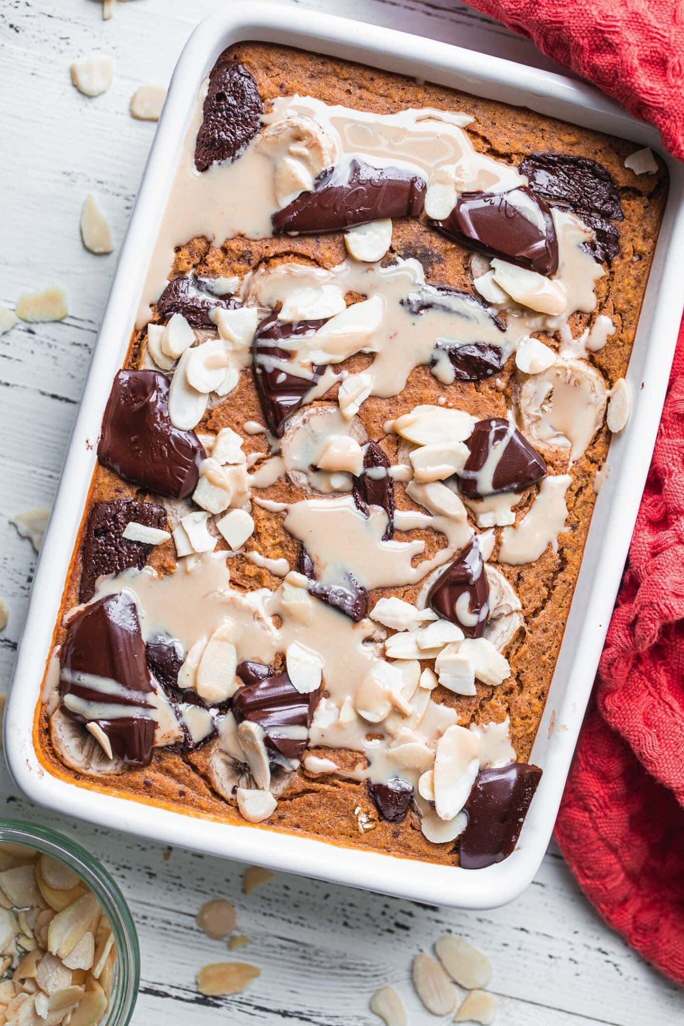 Vegan pumpkin baked oatmeal in a white baking dish with dark chocolate and sliced almonds