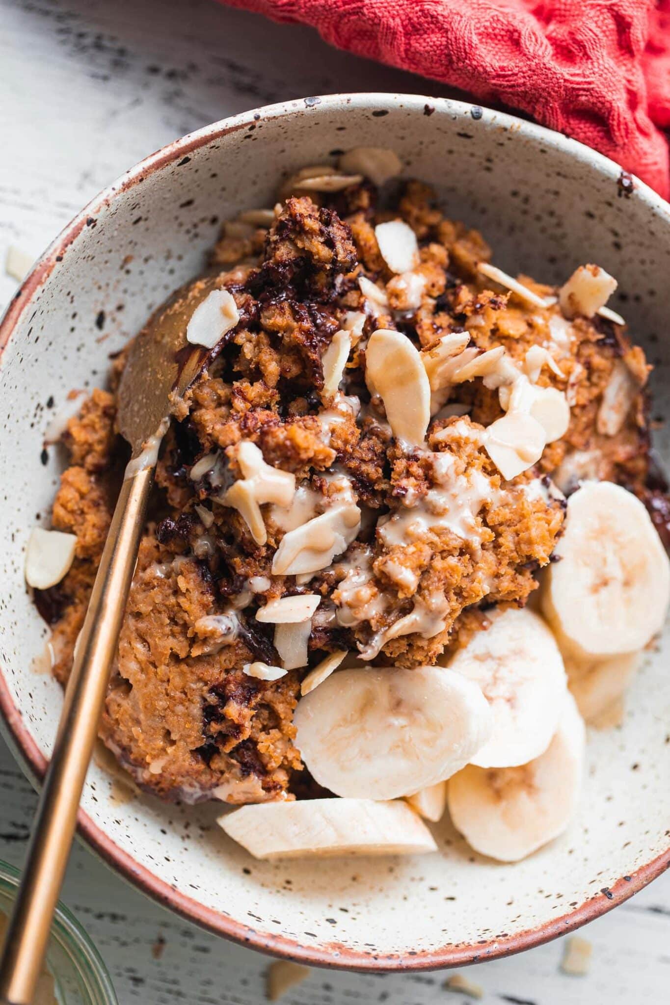 Bowl of pumpkin baked oats with banana slices, sliced almonds and a spoon