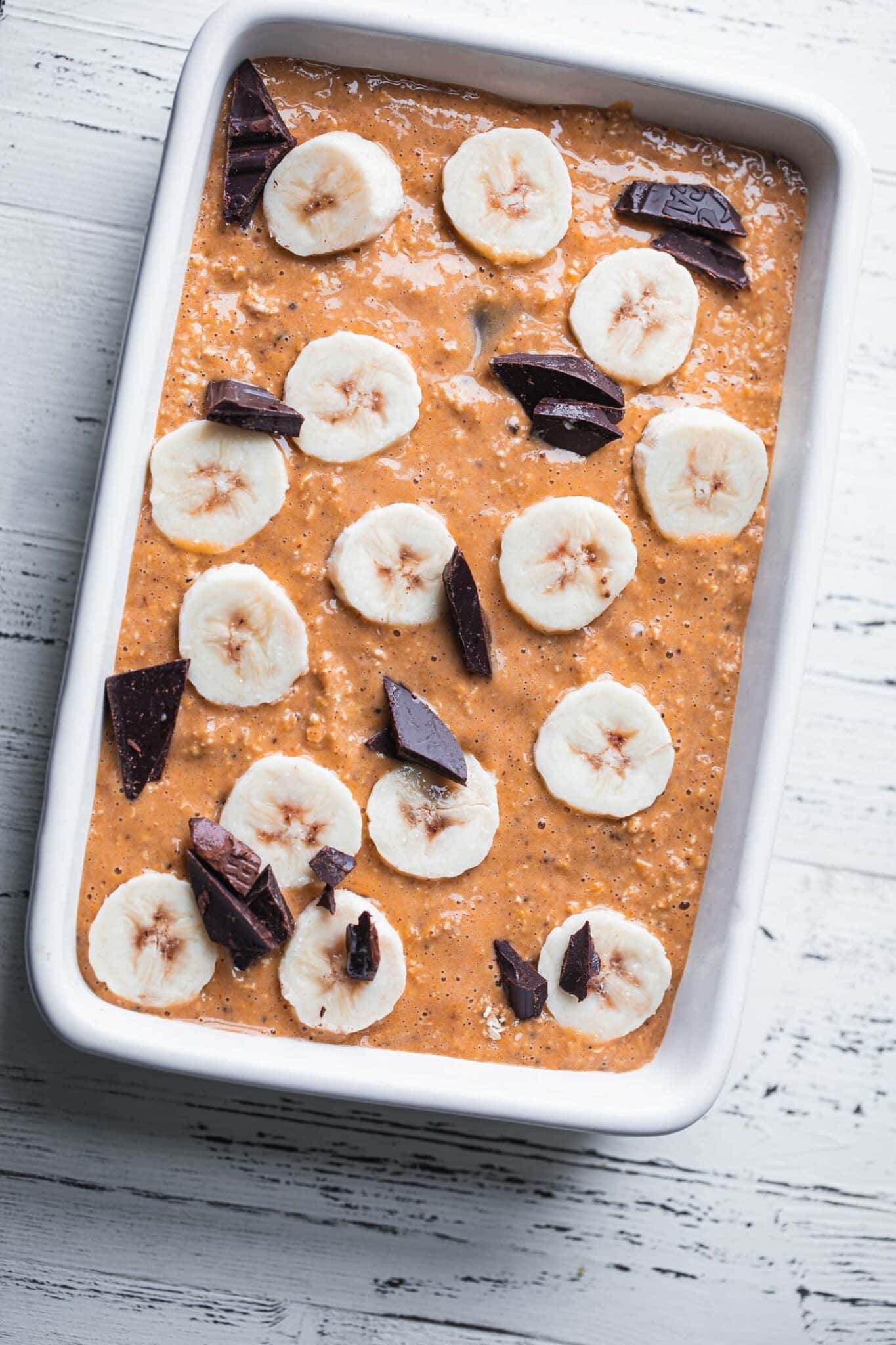 Unbaked pumpkin oats in a baking dish topped with banana slices and dark chocolate