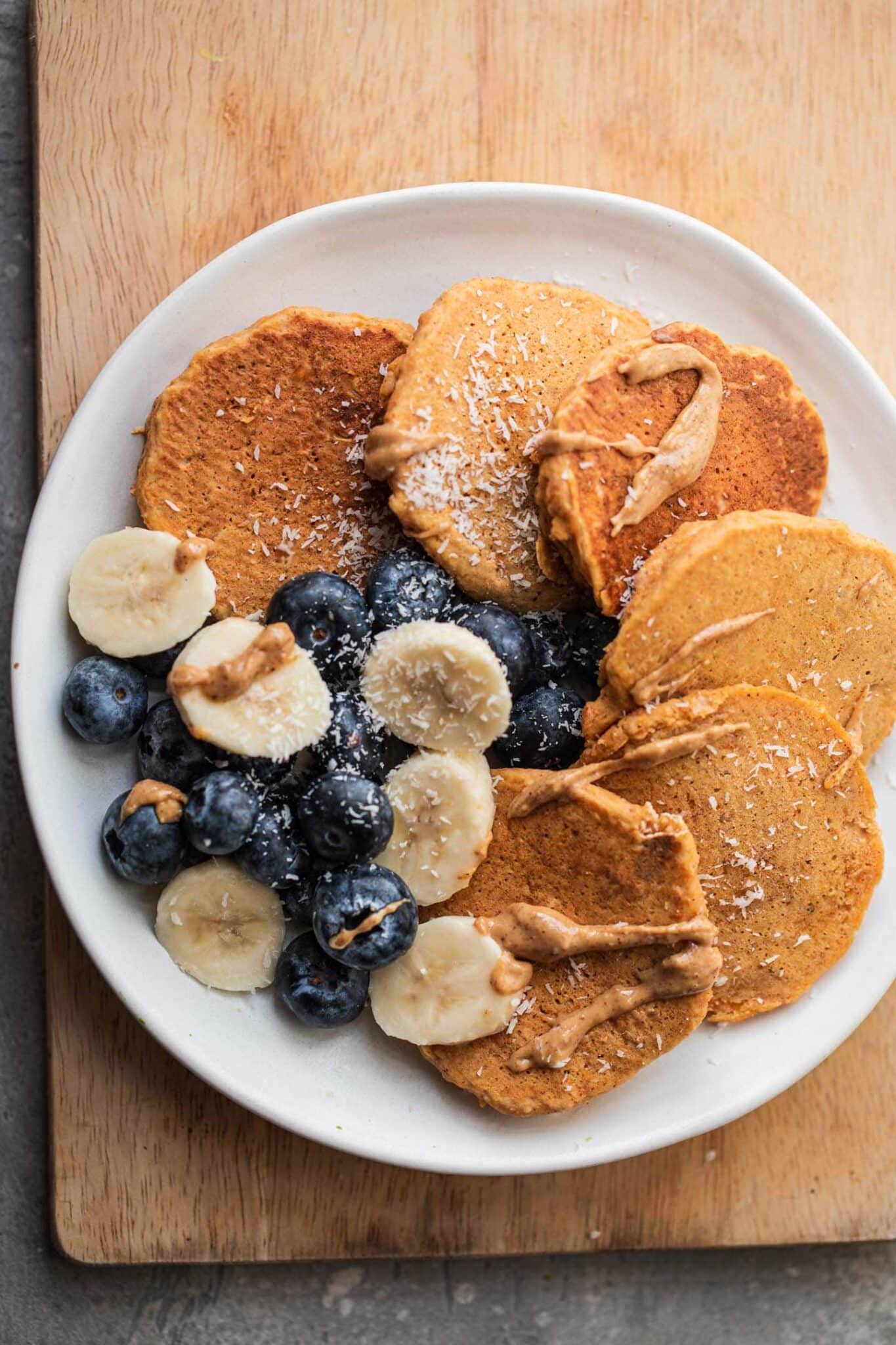 Pumpkin pancakes on a plate with fresh fruit and almond butter drizzle
