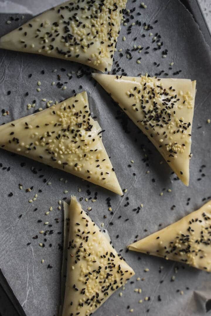 Samosas with sesame seeds on a baking tray