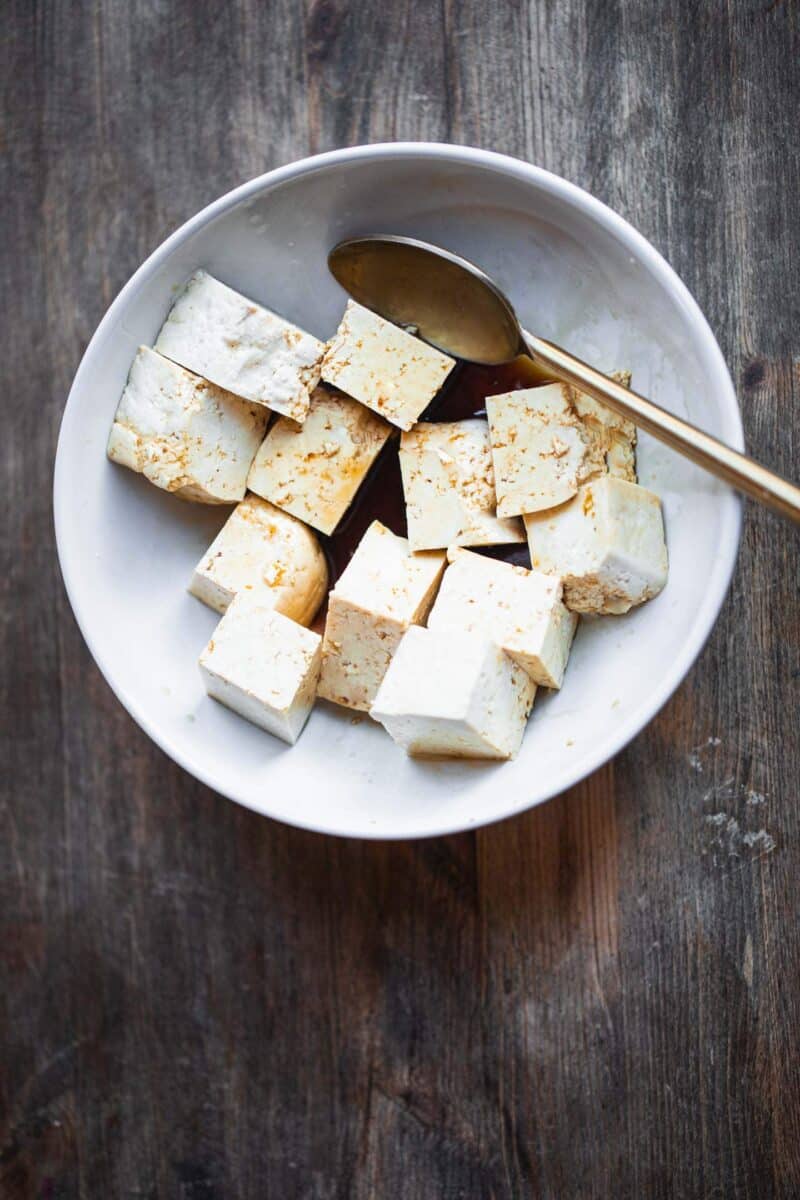 Tofu cubes in a marinade in a mixing bowl