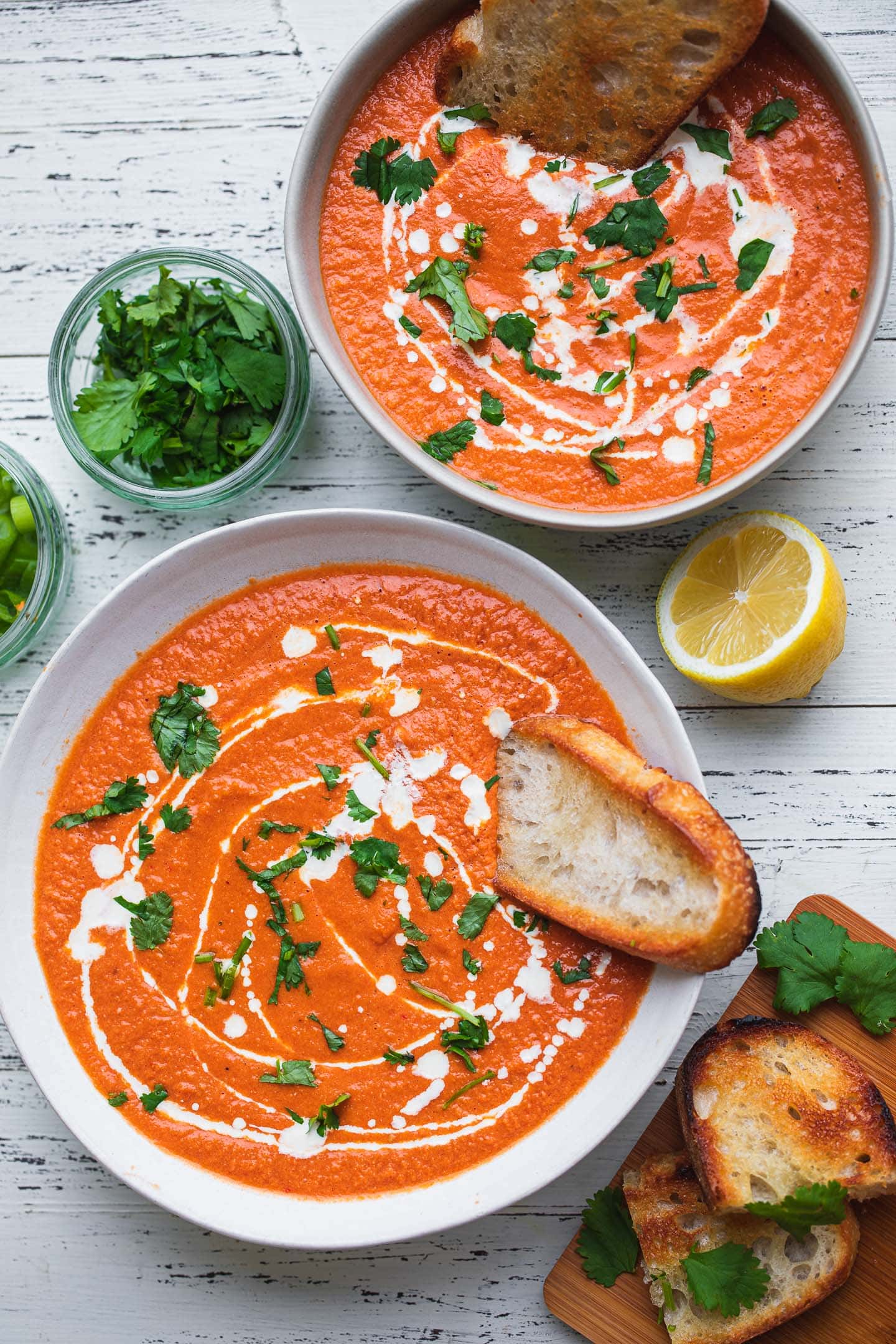 Two bowls of dairy-free tomato bisque with bread and cilantro