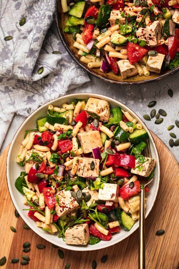 Two bowls of vegan pasta salad with vegetables and fresh herbs