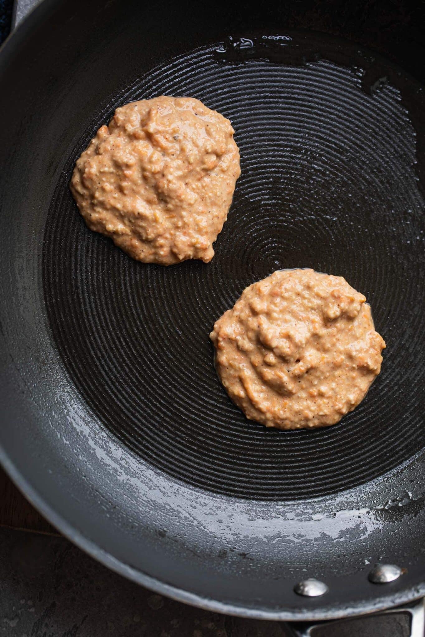 Two pumpkin pancakes cooking in a non-stick frying pan
