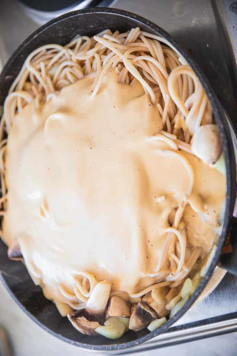 Vegan spaghetti in a frying pan with a creamy Alfredo sauce on top
