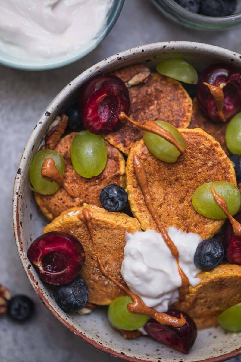 Closeup of a bowl of vegan sweet potato pancakes with soy yoghurt and berries