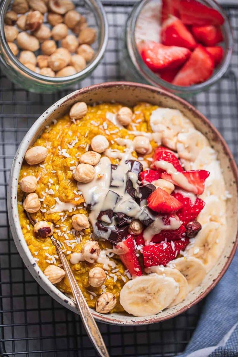 Bowl of vegan oats made with grated carrot and bananas, berries, nuts and chocolate as toppings