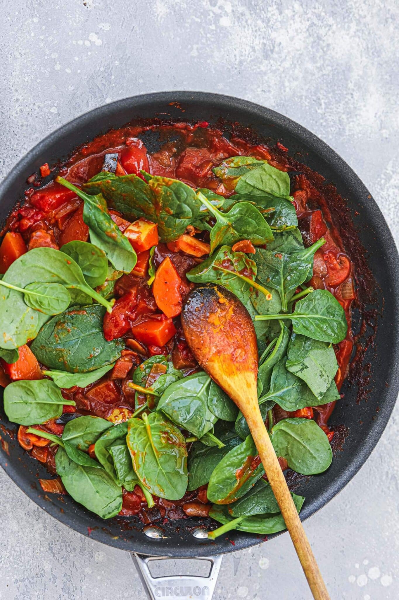 Vegan butternut squash curry in a frying pan with fresh spinach wilting on top