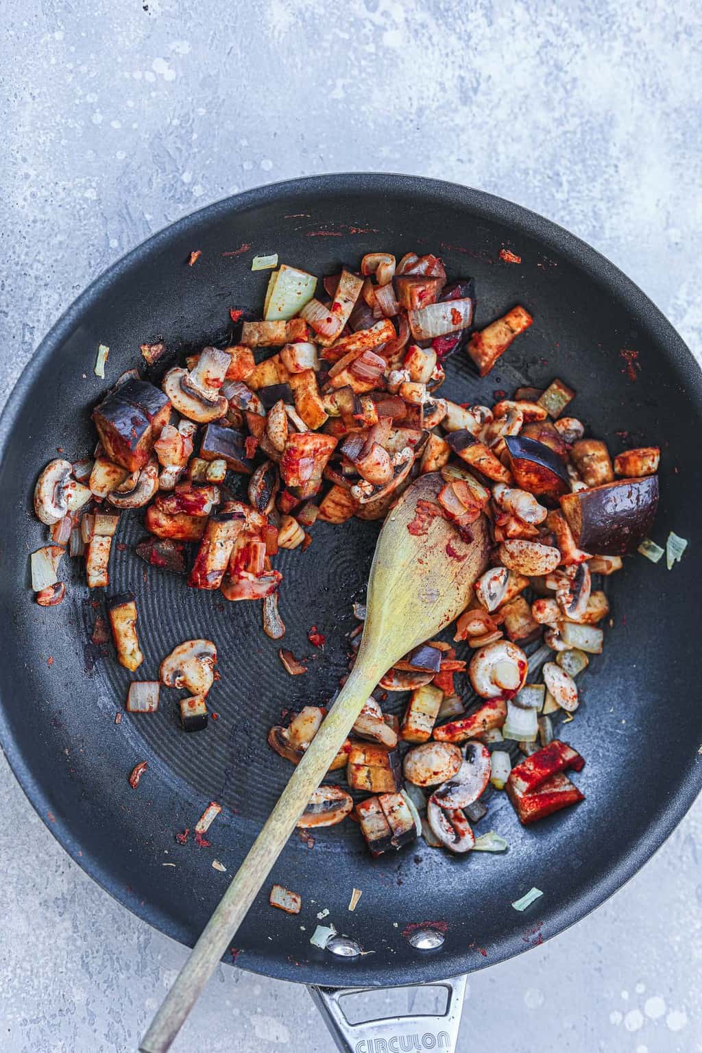 Eggplant, mushrooms and onion sauteing in a non-stick skillet with a wooden spoon