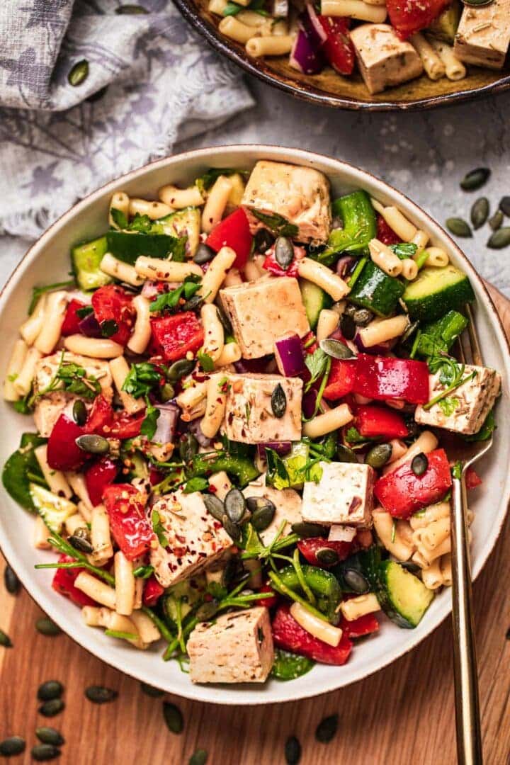 Vegan pasta salad with tofu feta and vegetables being served in a large bowl