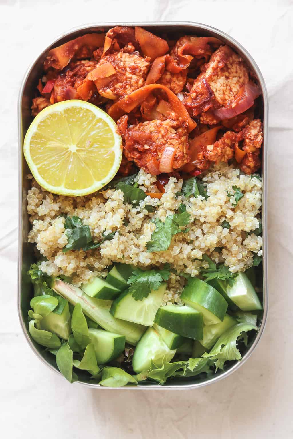 Vegan meal prep lunchbox with quinoa and tempeh in a tomato sauce