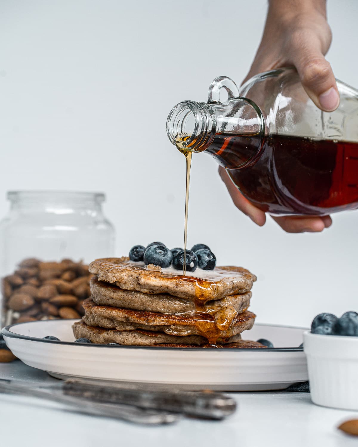 pouring maple syrup onto a stack of simple vegan pancakes topped with blueberries