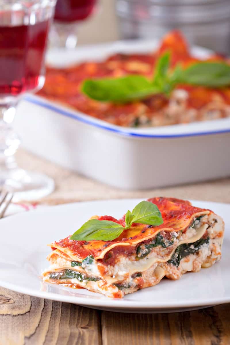 vegan lasagna on a white plate with larger casserole in the background