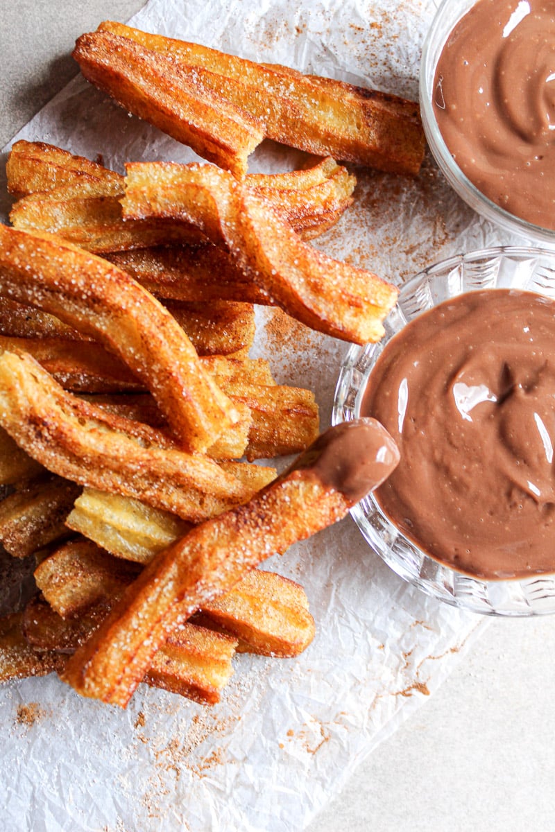 stack of homemade churros next to two bowls of melted chocolate 