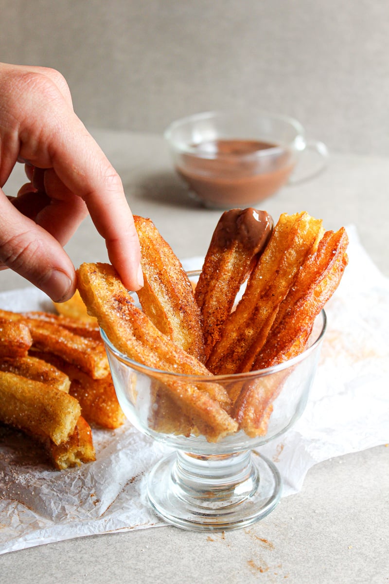hand grabbing for homemade churros in a glass cup 