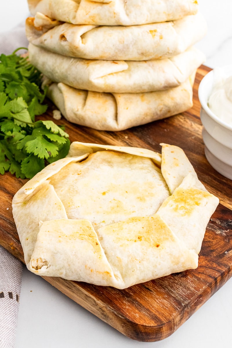 one un-cut vegetarian black bean crunch wrap supreme in front of a larger stack on wooden cutting board