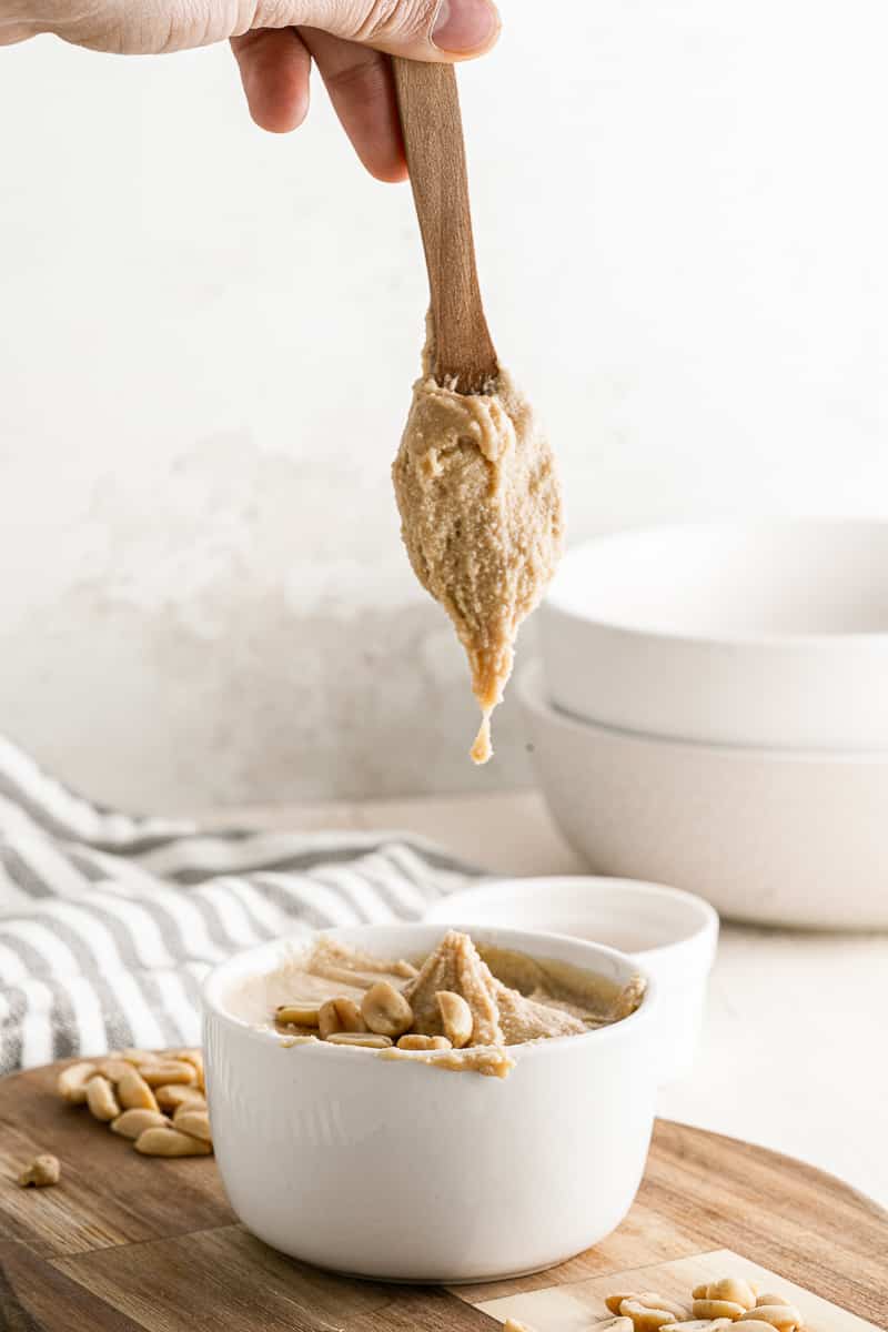 wooden spoon dipping out of small white bowl of 5-minute homemade peanut butter topped with peanuts