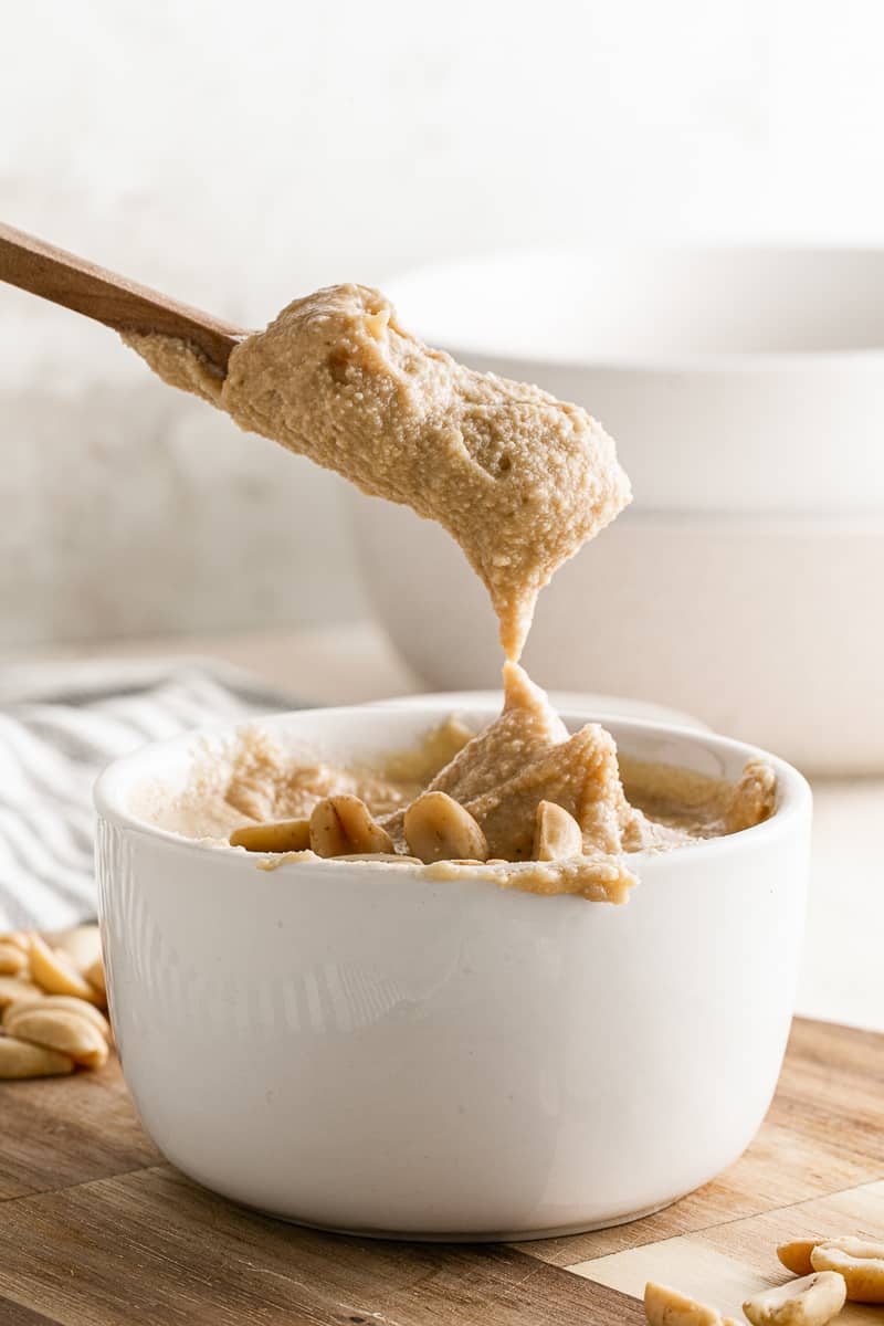 scoop of 5-minute homemade peanut butter on wooden spoon above white bowl 