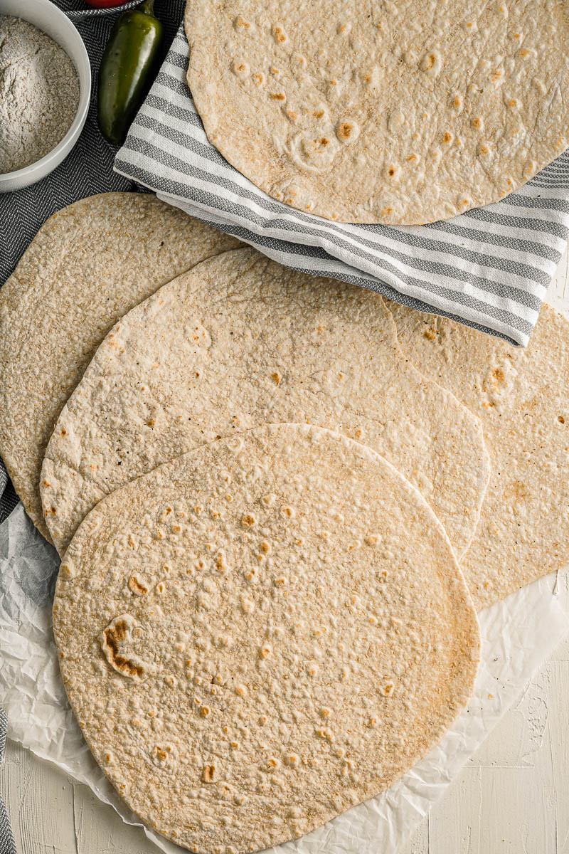 homemade tortillas stacked on a table on top of various dish towels