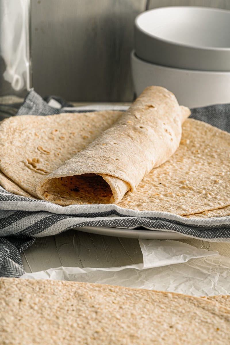 rolled tortilla on top of stacked homemade tortillas on a plate