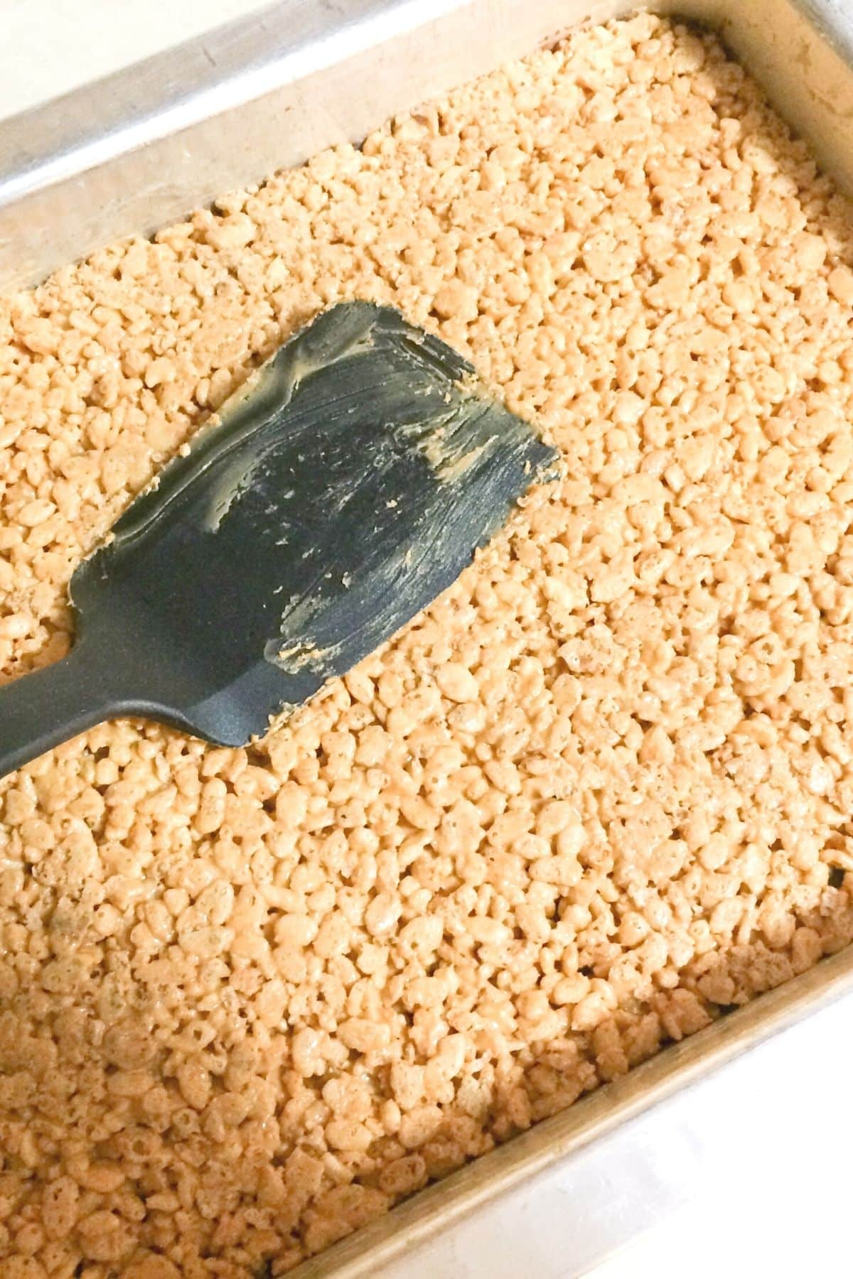 black spatula being used to flatten vegan rice krispie treats mixture into casserole dish
