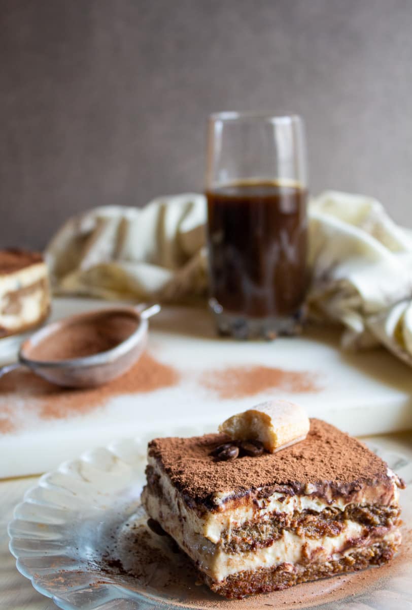 slice of best homemade tiramisu on clear plate and topped with coffee beans