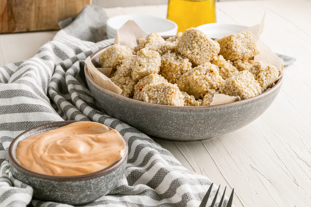 bowl of crispy sesame tofu cubes next to small bowl of sriracha mayo