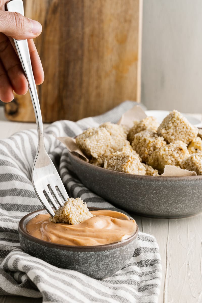 fork dipping one crispy sesame tofu into a bowl of dip
