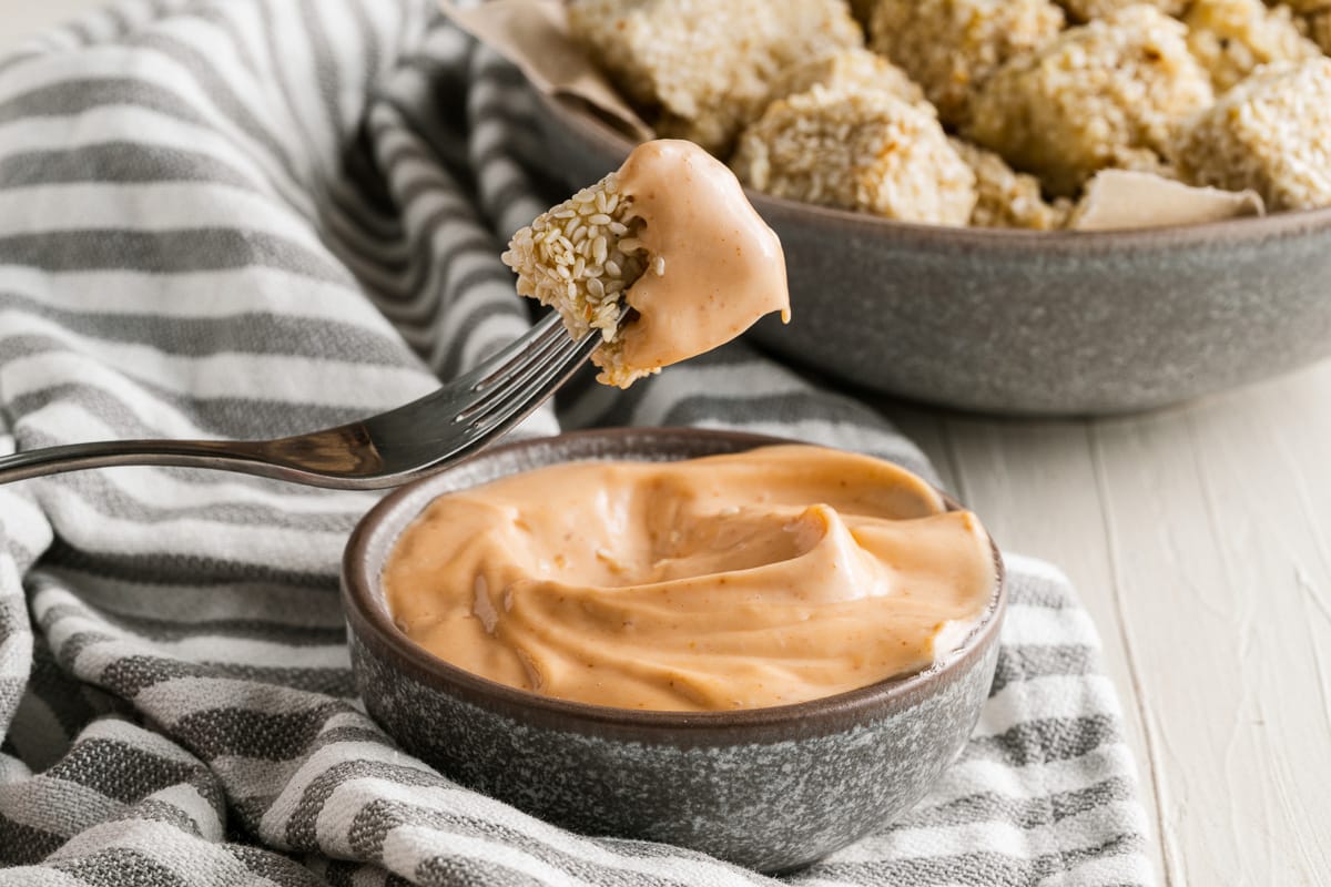 fork pulling dipped cube of crispy sesame tofu out of sriracha mayo dip