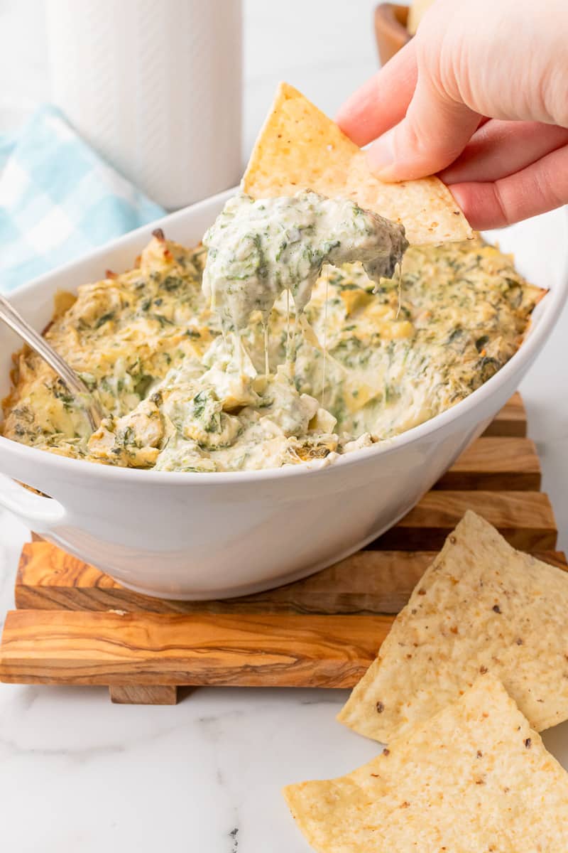 tortilla chip dipping out of white bowl of baked spinach artichoke dip without mayo