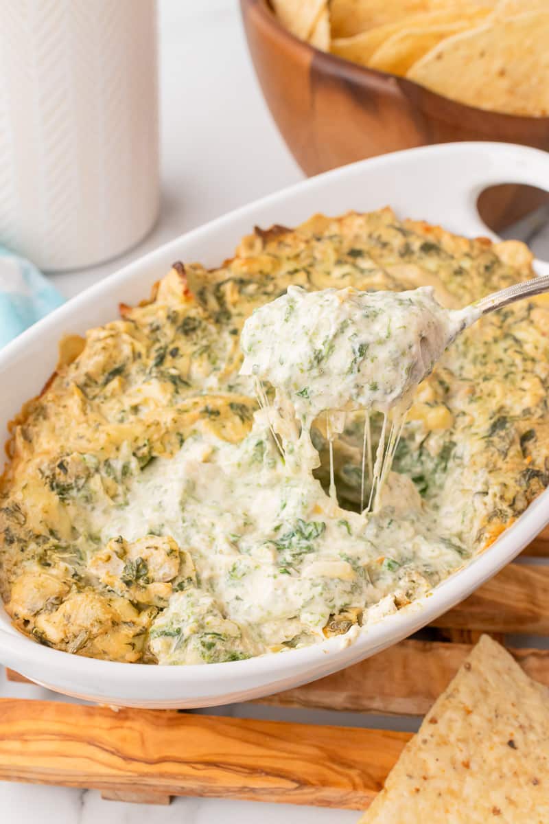 metal spoon scooping baked spinach artichoke dip without mayo out of white casserole dish