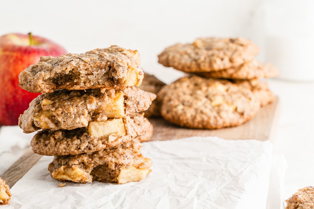 vegan apple oatmeal cookies stacked on a square of wax paper with apple in background