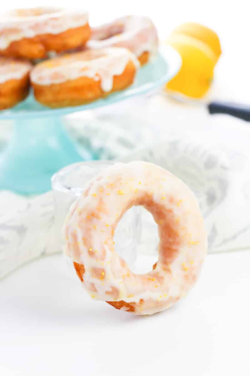 glazed lemon donut supported in a clear glass with stacked donuts in the bottom