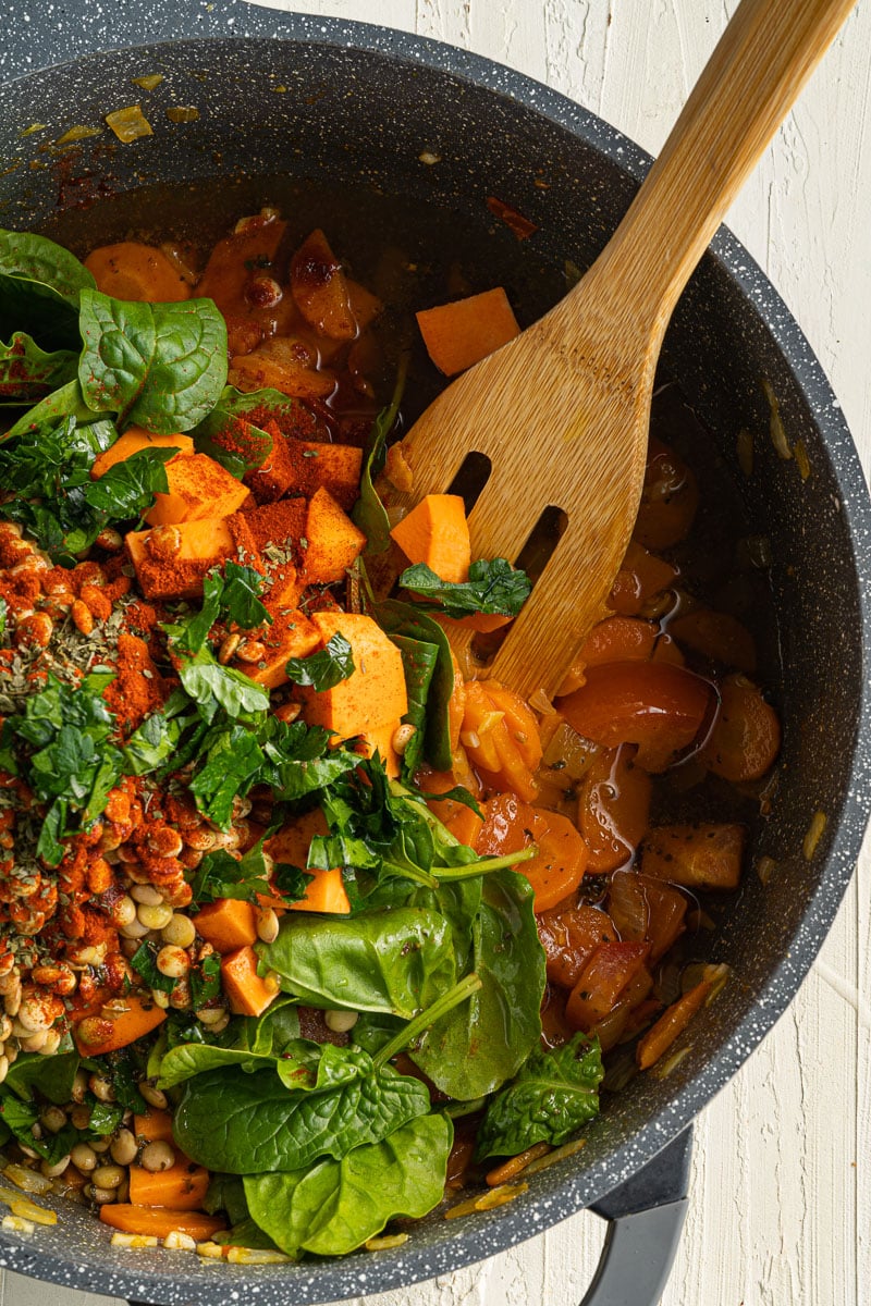 ingredients for one-pot sweet potato lentil stew in a large pot with wooden spoon